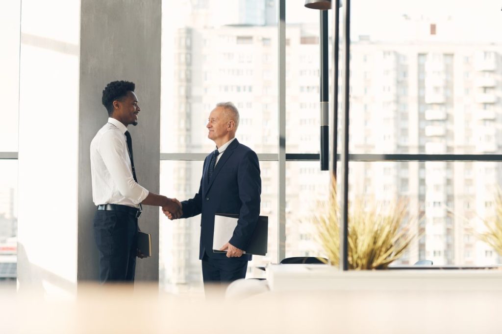 Senior recruiter with papers shaking hand of young Afro-American specialist while hiring him for work