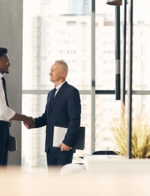 Senior recruiter with papers shaking hand of young Afro-American specialist while hiring him for work