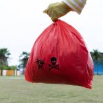 Woman holding red Bag Hazardous waste on the Park. Woman wearing yellow gloves holding red bag