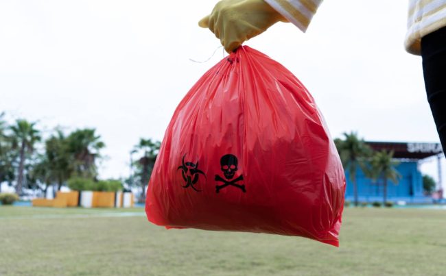 Woman holding red Bag Hazardous waste on the Park. Woman wearing yellow gloves holding red bag
