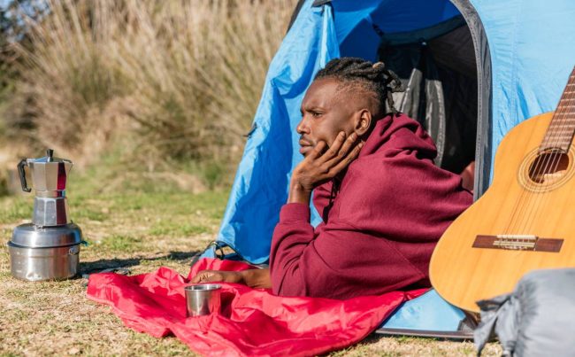 african american man lying down in camping tent relaxing in the wilderness
