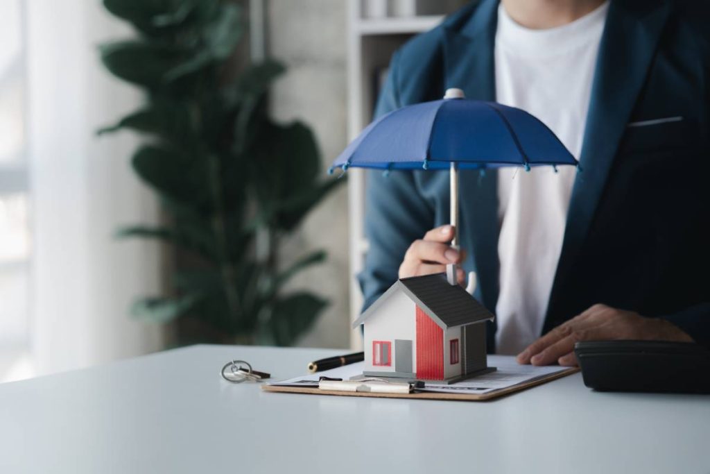 Individuals holding small umbrellas and model homes, housing insurance against impending loss and fire, building fire insurance, home and real estate insurance concepts.