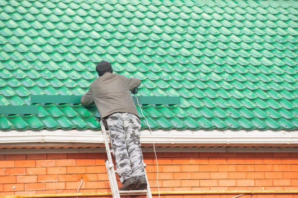 an adult man with his own hands installs snow removals on the roof of his house, preparing the house for a snowy cold winter