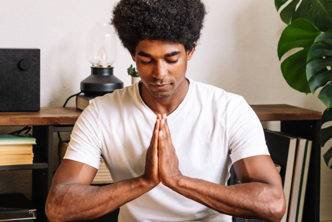 A black man with curly hair meditating with his eyes closed