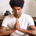 A black man with curly hair meditating with his eyes closed