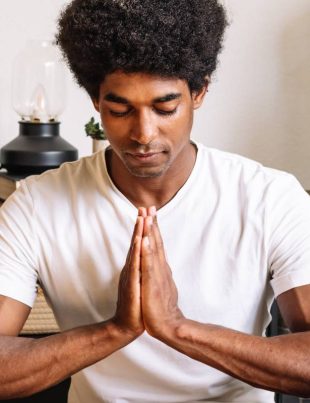 A black man with curly hair meditating with his eyes closed