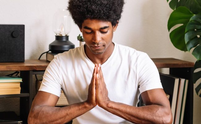 A black man with curly hair meditating with his eyes closed
