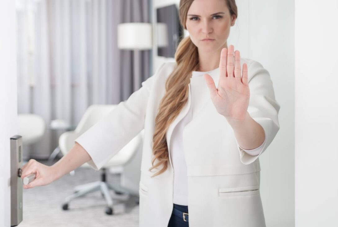 Young pretty woman standing in doorway and making stop sign with her hand