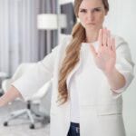 Young pretty woman standing in doorway and making stop sign with her hand