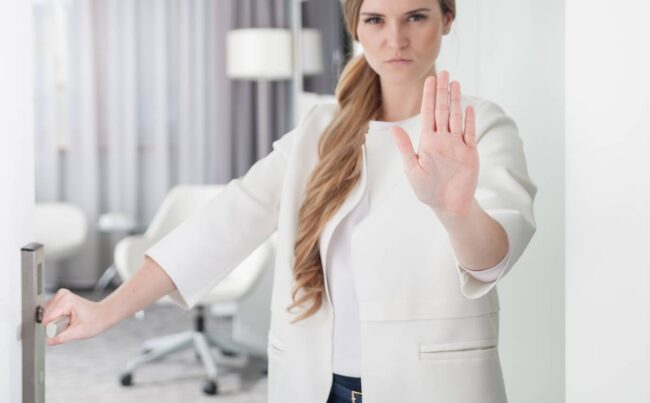 Young pretty woman standing in doorway and making stop sign with her hand